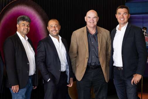 Four men in business casualwear stand in a line smiling